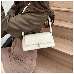 Detail of white crocodile pattern shoulder bag with a gold buckle on model's outfit
