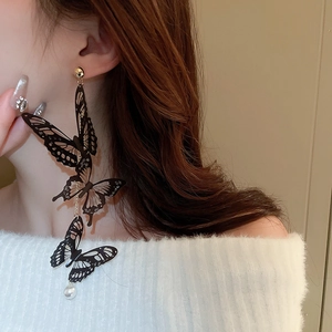 Détail de boucles d'oreilles papillon avec pampilles noires et perle portées par un mannequin