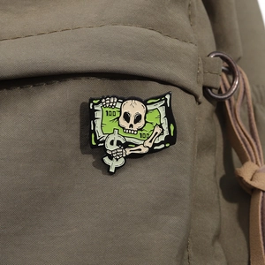 Macro shot of skull money tree enamel pin with dollar signs pinned to khaki fabric
