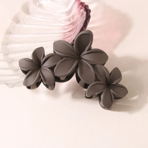 Matte dark grey triple flower hair claw clip displayed on glass plate for women