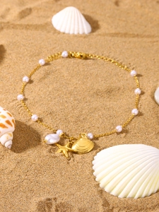 Macro detail of gold sea shell starfish anklet with white pearls on beach sand