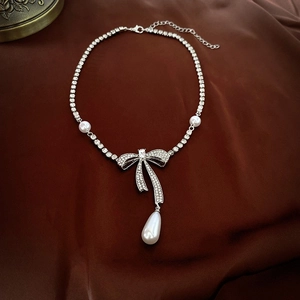 Macro view of silver bow necklace with rhinestones and teardrop pearl on brown silk