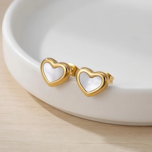 Dettaglio di orecchini a cuore dorati con inserto in madreperla su piatto ceramico