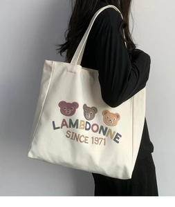 Detail of embroidered bear motifs and lettering on the beige canvas tote bag