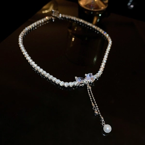 Macro detail of silver necklace featuring a rhinestone bow pendant and teardrop pearl