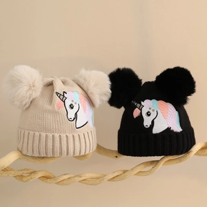 Detail von beigen und schwarzen Einhorn-Strickmützen mit flauschigen Doppelbommeln