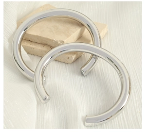 Macro detail of polished silver stainless steel C-shaped cuff bracelets on textured stone