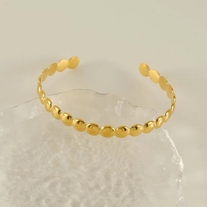 Close-up of golden disc link bangle with polished finish on a minimalist background
