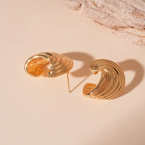 Macro detail of gold C-shaped earrings with shell texture on a neutral stone background