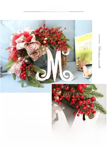 Detail of Christmas wreath with white letter M, red berries, pine cones and rustic bells