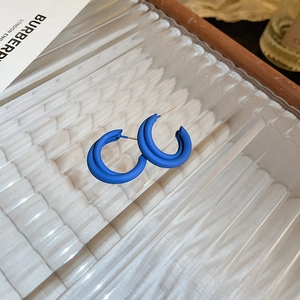Macro side view of blue matte double-layered C-shaped hoop earrings on a textured plate