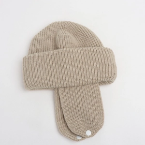 Close-up of beige knitted kids hat showing ribbed texture and metal earflap fastener