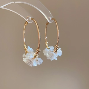 Detail of gold hoop earrings featuring white floral clusters and small metallic beads