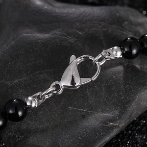 Macro shot of stainless steel clasp and black beads on a textured stone background