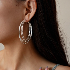 Nahaufnahme eines Models mit mehrlagigen silbernen Reifenohrringen und Metallic-Finish