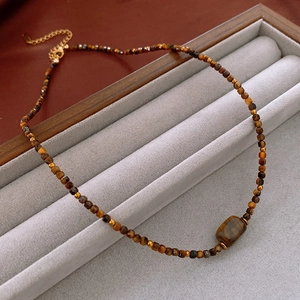 Macro detail of faux tiger eye beaded necklace with rectangular stone pendant in jewelry tray