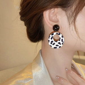 Close-up of leopard print acrylic round pendant earrings worn by a model in warm light