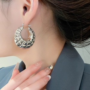Detail of silver hoop earring with hammered texture on a model wearing a blue blazer