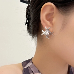 Detail of silver geometric cross earrings with central sphere on female model ear