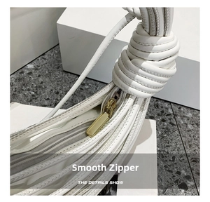 Dettaglio della zip dorata e del manico annodato bianco sulla borsa minimalista