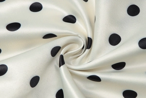 Dettaglio del tessuto in raso liscio con pois neri classici su base color crema