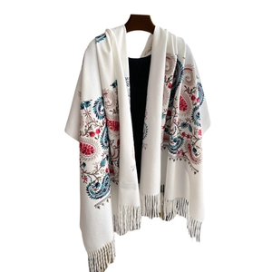 Châle blanc brodé de motifs paisley colorés avec de longues franges présenté sur un cintre