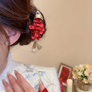 Detail of fish-shaped hair clip with red sequins and blue gemstone on model