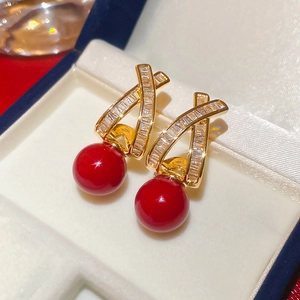 Macro detail of gold-plated cross earrings with clear zircon stones and red sphere charms