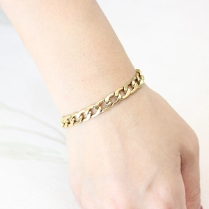 Polished gold stainless steel thick Cuban curb chain bracelet worn on a female wrist