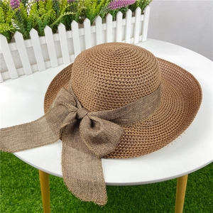 Detail of a brown woven straw sun hat with a large textured bow on a white table