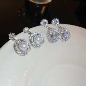 Detailed shot of silver pearl flower earrings and crystal zircon studs on white ceramic