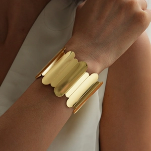 Detailed view of wide gold metal cuff bracelet with geometric spliced plates on wrist