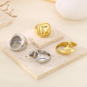 Minimalist square 18K gold and silver stainless steel rings displayed on beige travertine