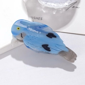 Close-up of a blue bird-shaped acetate hair claw clip with black spots and yellow eye detail