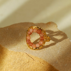 Detail of gold titanium ring with orange natural stone beads on a rustic stone base