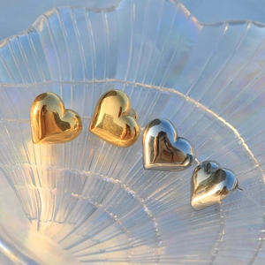 Polished heart stud earrings in gold and silver finish on a shell glass tray