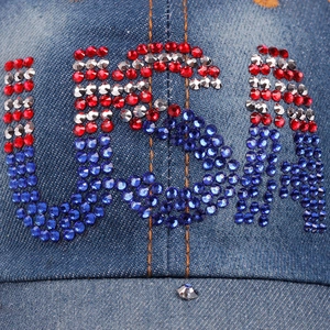 Close-up of a blue denim baseball cap featuring 'USA' in sparkling red, white, and blue rhinestones.