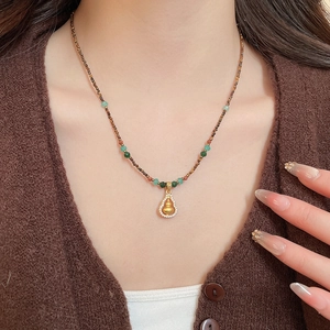 Detailed view of gourd pendant necklace with tiger eye beads on brown knitwear