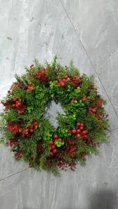 Detail of Christmas wreath with green cypress leaves and vibrant red berries on gray tile