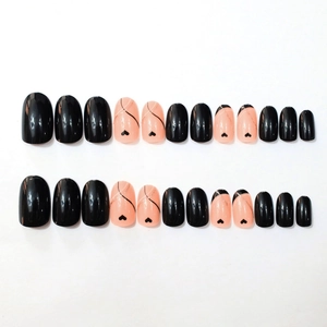Press-on nail set with black heart patterns and glitter accents on nude pink base