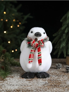 Detail of white flocked Christmas penguin ornament with knit scarf on snow-covered wood