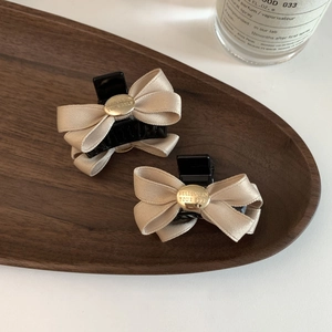 Detail of satin bow hair claws in beige and black with engraved metal buckle detail