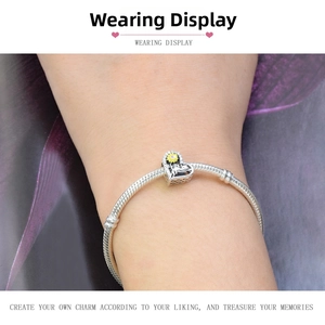 Detail of silver snake chain bracelet with heart charm and yellow enamel flower