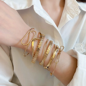 Detailed view of layered gold bangle set with wave and bow designs on a female wrist
