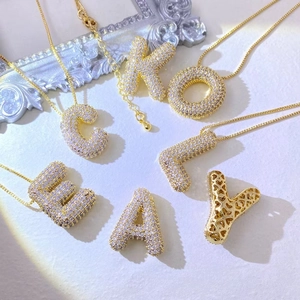 Gold bubble letter pendant necklace with sparkling cubic zirconia on a white background