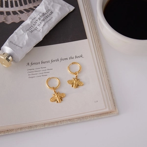 Detail of 18K gold stainless steel bee hoop earrings on an open book page