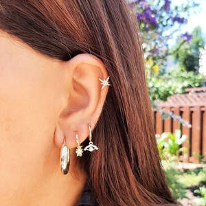 Close-up of S925 silver needle earrings with star and eye charms on model's ear
