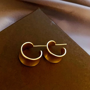 Macro view of golden C-shaped hoop earrings with matte brushed metallic finish detail