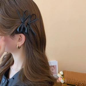 Detail of Y2K faux leather black bow hair clip worn by model with gold hoop earrings