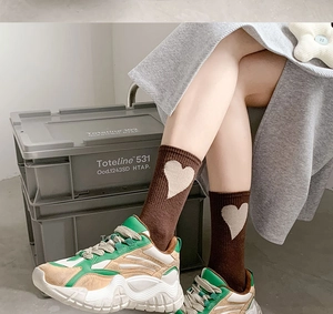 Detail of brown cotton crew sock with cream heart pattern paired with retro sneakers